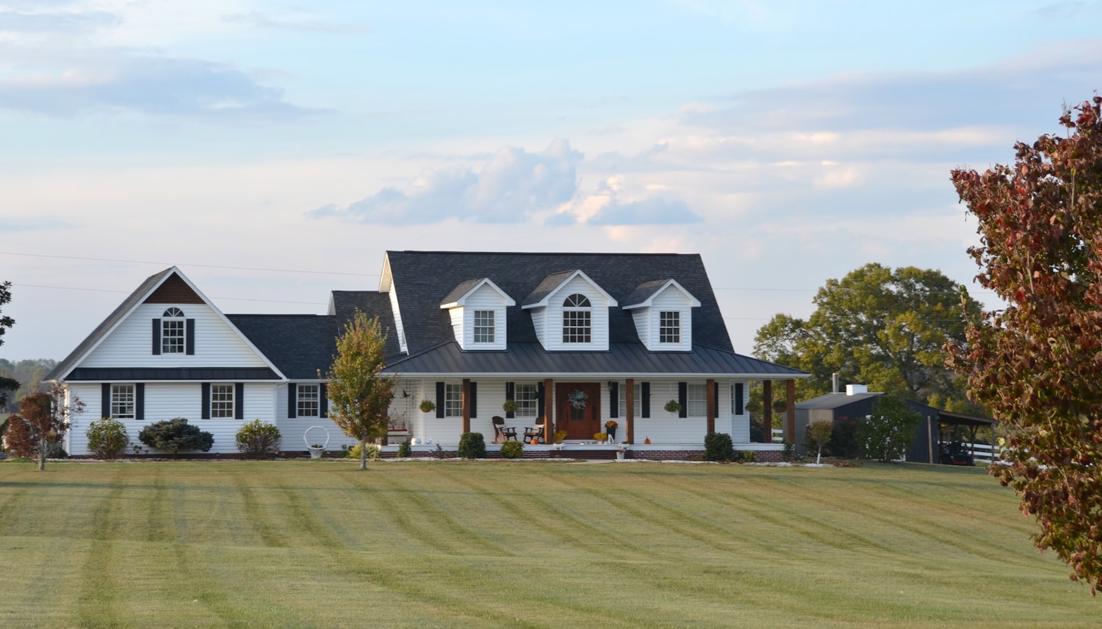 White farmhouse with a wraparound porch surrounded by trees